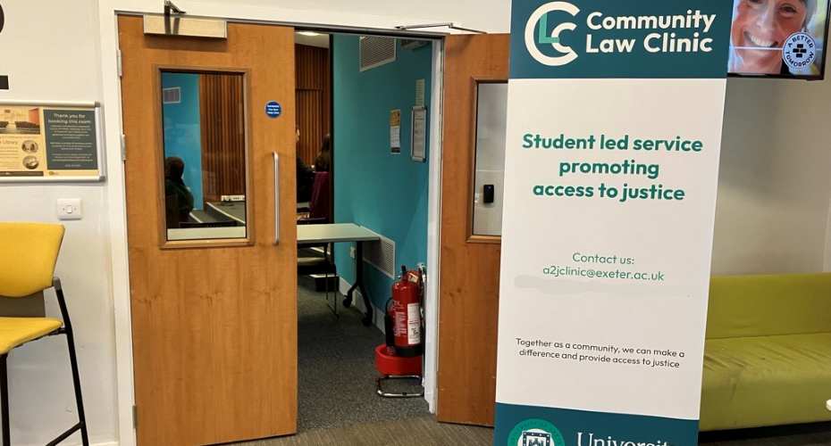 A pull up sign displaying the Community Law Clinic logo. Student led service promoting access to justice. Contact us: a2jclinic@https-exeter-ac-uk-443.webvpn.ynu.edu.cn, Together as a community, we can make a difference and provide access to justice. It is stood in front of an open door to the room called Rougemont.